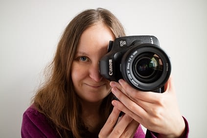 Catherine Tuckwell Personal Brand Photography holding camera to eye while smiling against white background